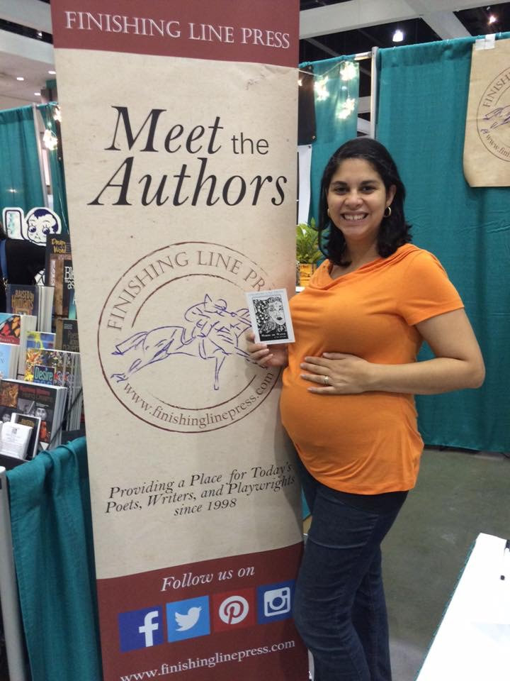 Picture of Li Yun Alvarado holding her pregnant belly and a postcard with a picture of the cover of her book Words or Water in front of a Finishing Line Press sign at AWP 2016.